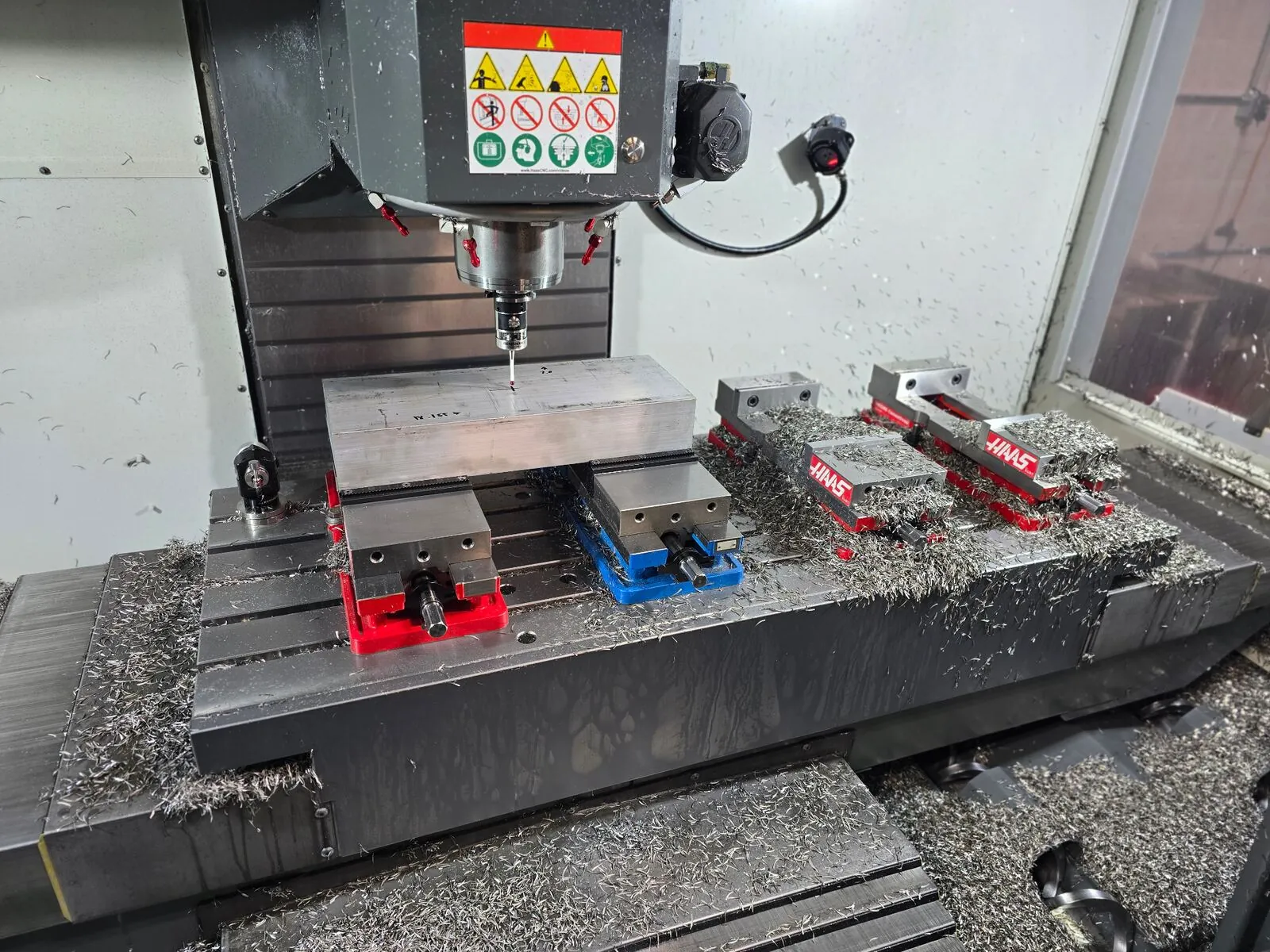 Haas CNC vertical machining center milling aluminum workpiece with multiple vises on T-slot table at Olympus Machining shop in Hanover Pennsylvania
